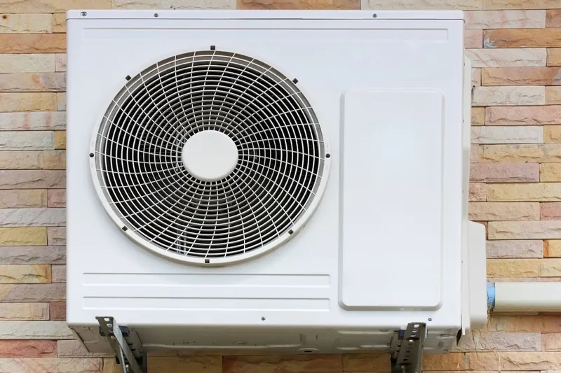 Aircon outdoor unit on wall brackets against a stone-clad wall