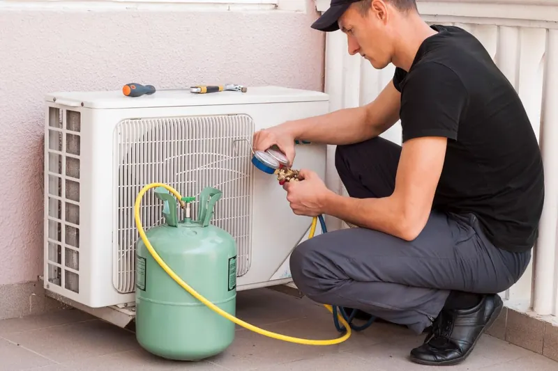 Technician checking refrigerant pressures on an outdoor aircon unit with a gauge set