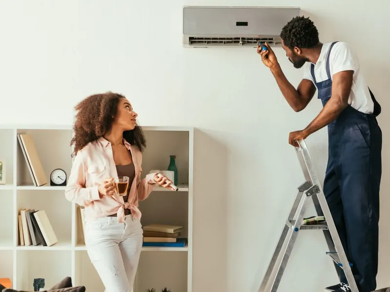 Technician checking a wall-mounted split air conditioner while the homeowner holds the remote