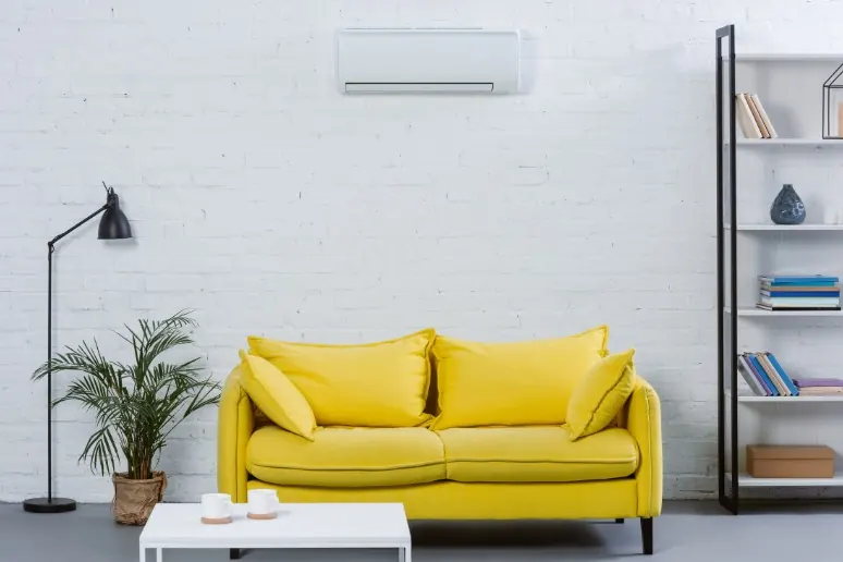 Wall-mounted split air conditioner above a sofa in a lounge